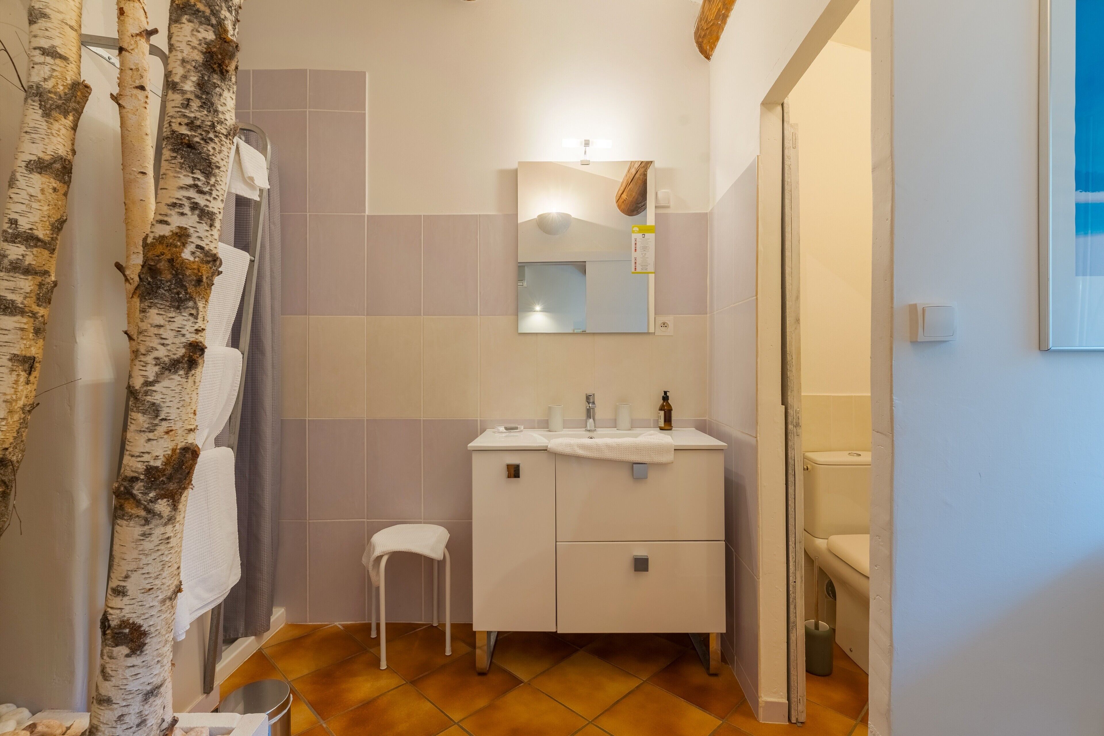 A bathroom with a white vanity, a mirror, a towel rack, and a small stool.