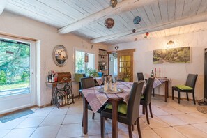 Un espace repas avec une table dressée pour quatre personnes, entourée de chaises, doté d’un plafond en bois et offrant une vue sur l’extérieur.