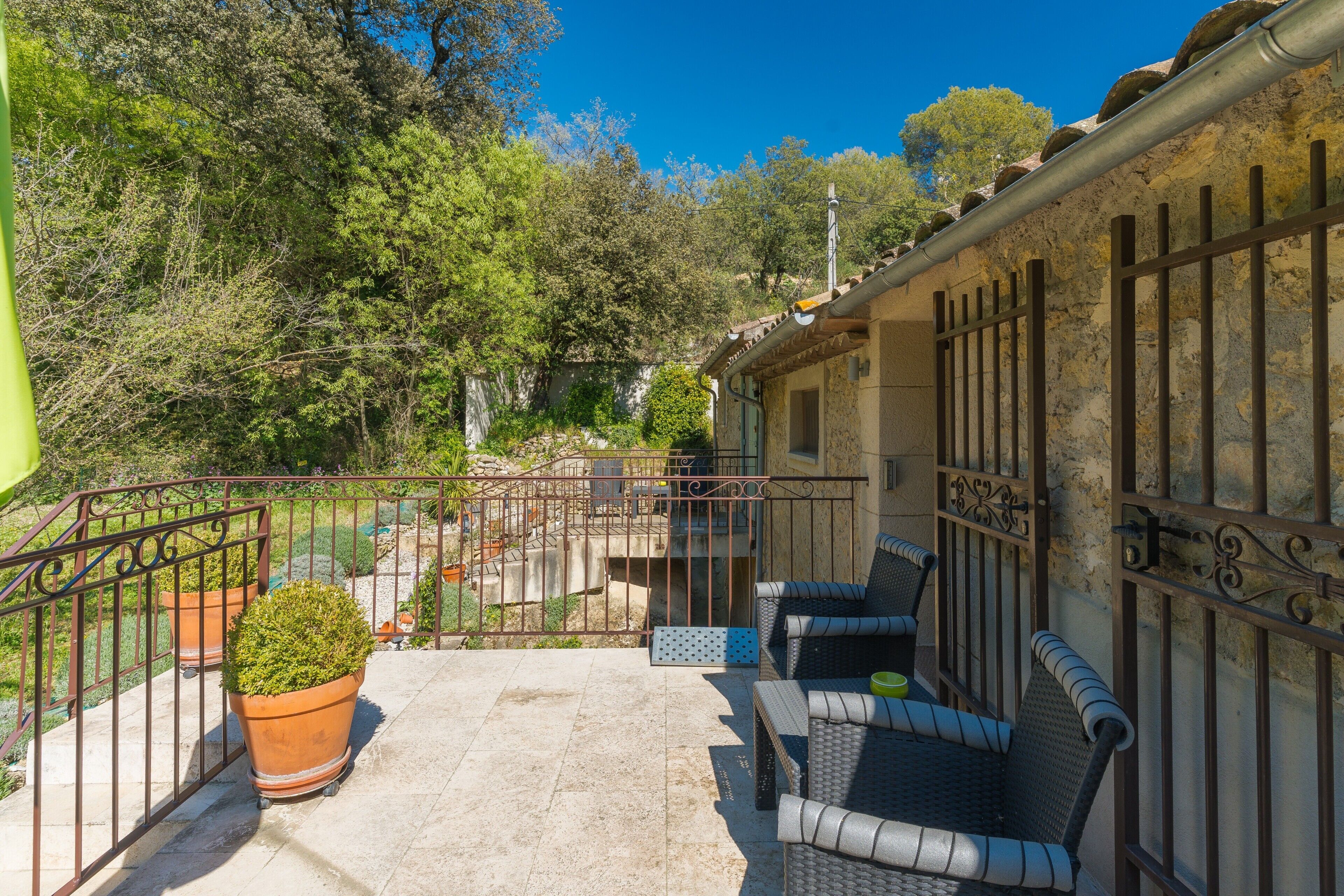 A balcony with outdoor furniture, potted plants, and a view of trees and a building.