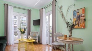 Una habitación con pared verde, suelo de madera, un sofá, una mesa con un florero, una silla y un cuadro.