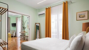Una habitación de hotel con cama, espejo, televisor y ventana con cortinas.