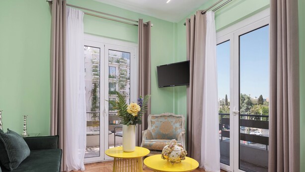 Una sala de estar con un sofá verde, mesas amarillas, un televisor y un balcón con vistas.