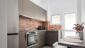 A modern kitchen with stainless steel appliances, a brick backsplash, and a dining area with a white table and chairs. - Hera Family Apartment, Olympian Zeus Apartments (Athens)