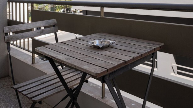 A balcony with a wooden table and chairs, a metal tray, and a view of a modern building with balconies. - Hera Family Apartment, Olympian Zeus Apartments (Athens)