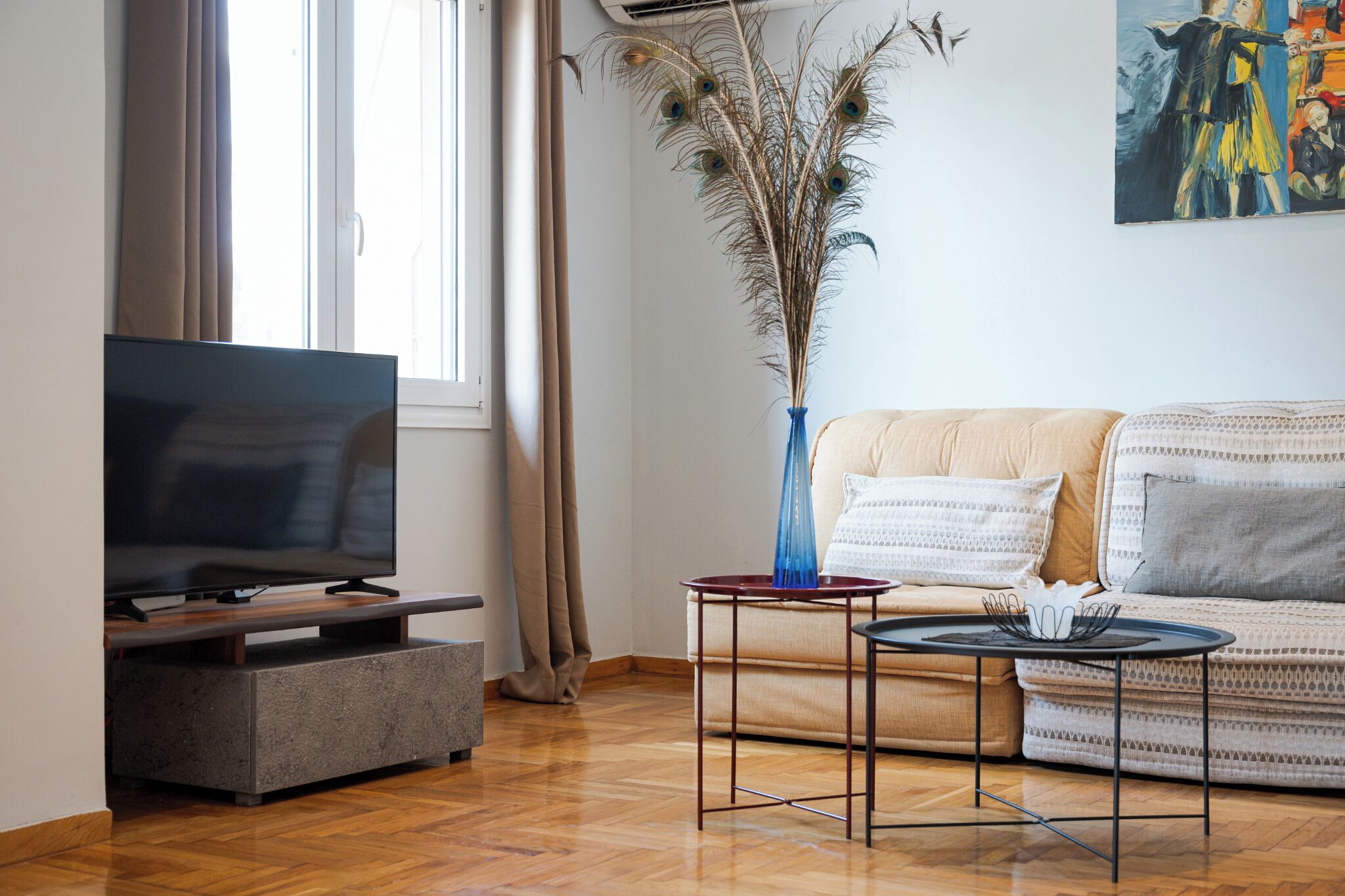 A living room with a flat-screen TV, a sofa, a coffee table, and a decorative vase with dried plants.