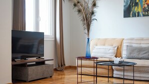 A living room with a flat-screen TV, a sofa, a coffee table, and a decorative vase with dried plants. - Zeus Grand Apartment, Olympian Zeus Apartments (Athens)