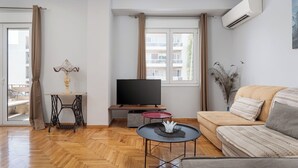 A modern living room with a sofa, a TV, a small table, and a window with curtains. - Zeus Grand Apartment, Olympian Zeus Apartments (Athens)