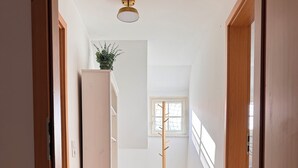 Un couloir étroit au plancher en bois, une armoire blanche, une plante posée sur le dessus, et un lampadaire.