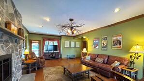 A cozy living room with a stone fireplace, leather sofas, a coffee table, and a television.