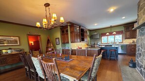 A spacious dining area with a large wooden table and chairs, a chandelier, and a kitchen with wooden cabinets and a stone accent wall.