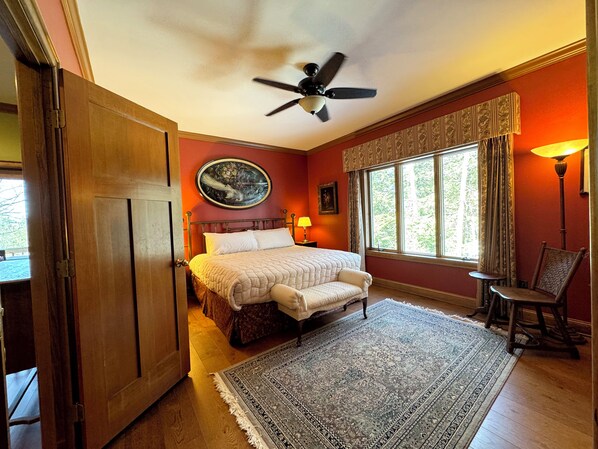 A bedroom with a bed, a nightstand, a chair, a window with curtains, a ceiling fan, and a rug. - The Lodge at Warner Bay, Lake George Retreat for Up to 20 People (Kattskill Bay)