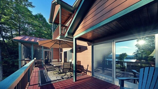 A modern house with a deck, outdoor seating, and a large glass door leading to a scenic view.