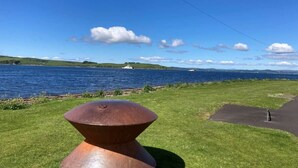 A grassy area with a metal sculpture, a paved path, and a body of water with boats in the distance. - The Waterside Apartment, ideal for families (Largs)