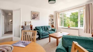 A cozy living room with a green sofa, a wooden coffee table, and a dining table with chairs. - The Waterside Apartment, ideal for families (Largs)
