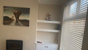 Une pièce avec une cheminée, un tableau représentant un éléphant, une statue et une fenêtre avec des stores.