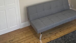 Une pièce avec un canapé gris, une porte blanche et un tableau accroché au mur.