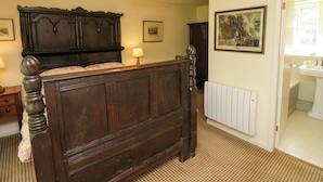 Un dormitorio con cama de madera, un radiador, un cuadro enmarcado en la pared y una puerta que da a un baño.