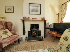 A living room with a fireplace, a sofa, a television, and a decorative shelf. - The Laundrymaid's Cottage (Grange-over-Sands)