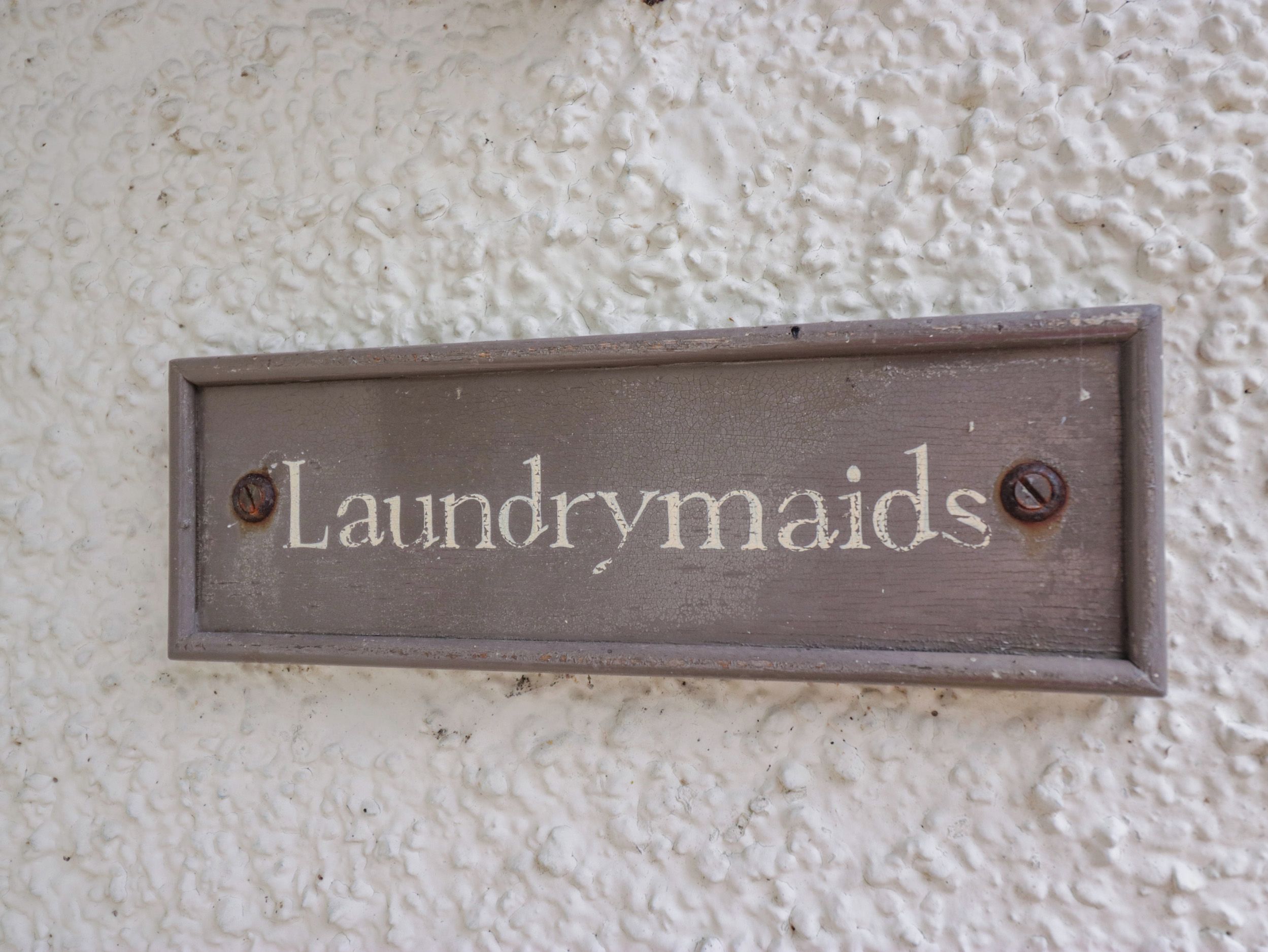 A wooden sign with the text 'Laundrymaids' mounted on a textured white wall.