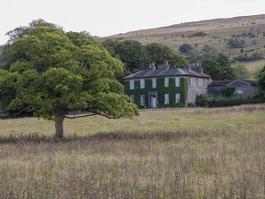 A large house with a green exterior, surrounded by a grassy field and a hill in the background. - The Laundrymaid's Cottage (Grange-over-Sands)