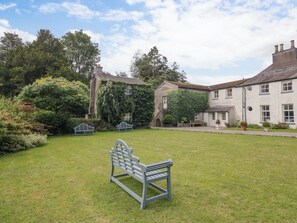 A grassy courtyard with a bench, a stone wall, and a building with a white facade and multiple windows. - The Laundrymaid's Cottage (Grange-over-Sands)