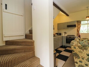 A kitchen with a gas stove, oven, and a window with curtains. There are steps leading to a door with a white frame. - The Laundrymaid's Cottage (Grange-over-Sands)