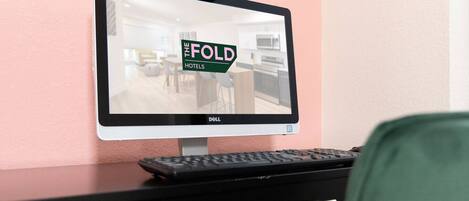 Un monitor de computadora muestra un interior de hotel con un letrero que dice 'THE FOLD HOTELS' en una pared rosa.
