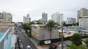 Un paisaje urbano con edificios modernos, una calle con coches estacionados y una persona trabajando en la acera.