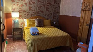 Una habitación con cama, mesita de noche, lámpara y puerta de madera.