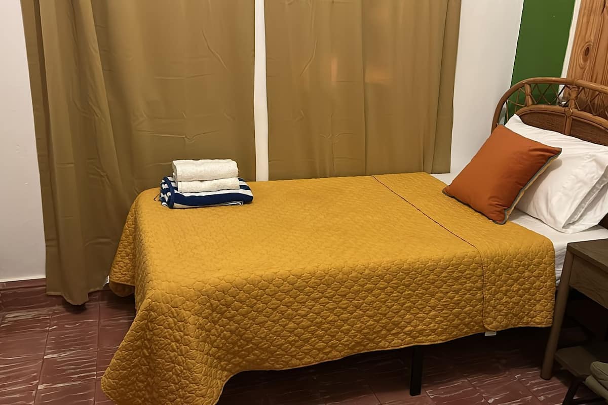 A single bed with a yellow quilt, a wooden headboard, and a brown pillow.