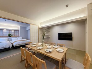 Una habitación de hotel moderna con zona de comedor, cama, televisión y una planta pequeña.