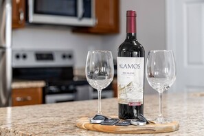 A bottle of Alamos Red Blend wine on a wooden coaster with two glasses beside it.
