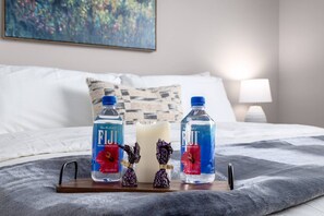 A bed with two bottles of Fiji water, a candle, and two decorative figures on a tray.