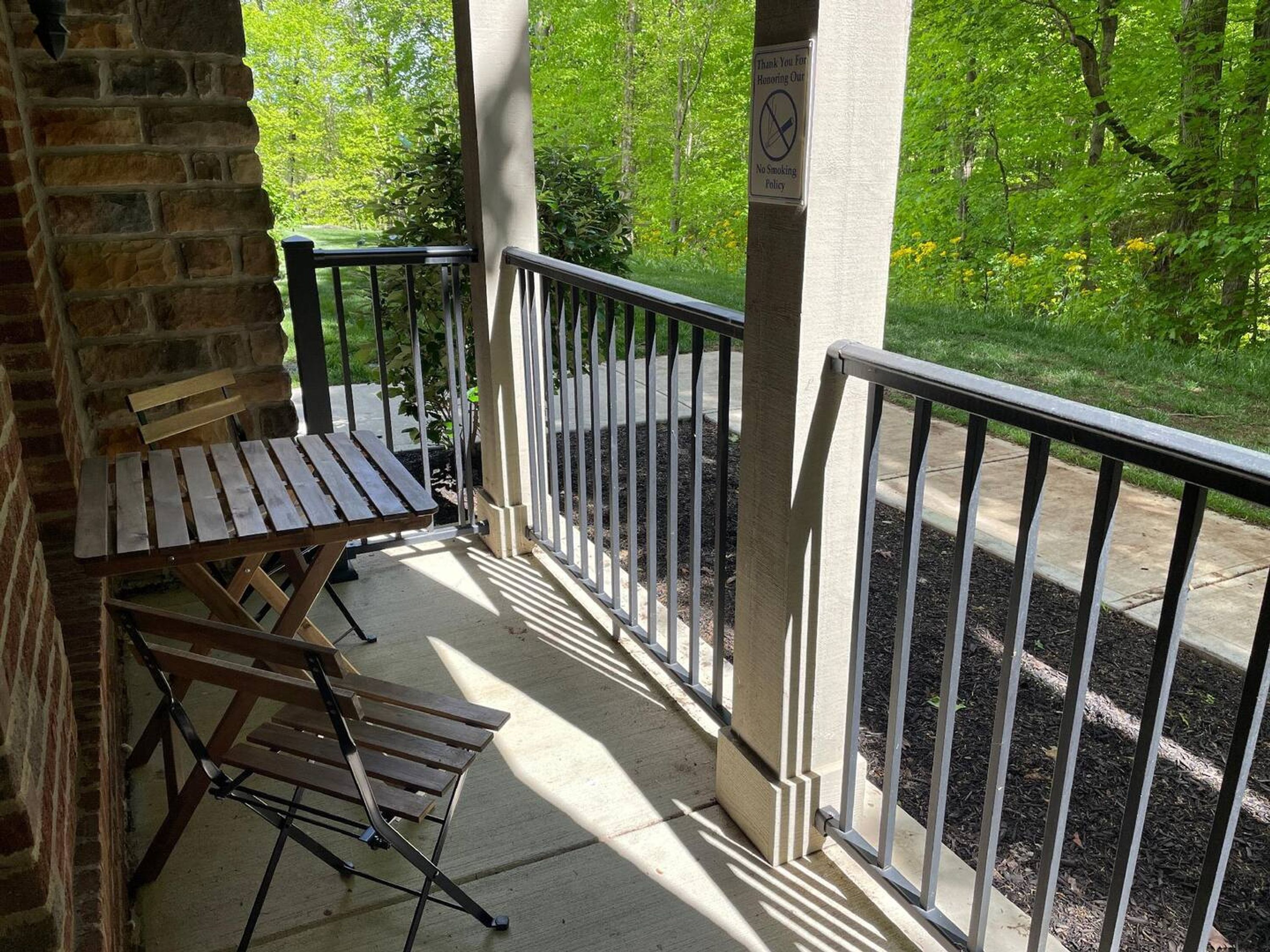A covered outdoor seating area with a wooden bench and a table, surrounded by a metal railing.