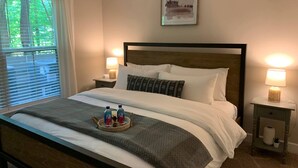 A neatly made bed with a headboard, two bedside lamps, a framed picture on the wall, and a tray with bottles and a candle on the bed. - Polaris King Flat Pet-friendly Nature Views (Westerville)