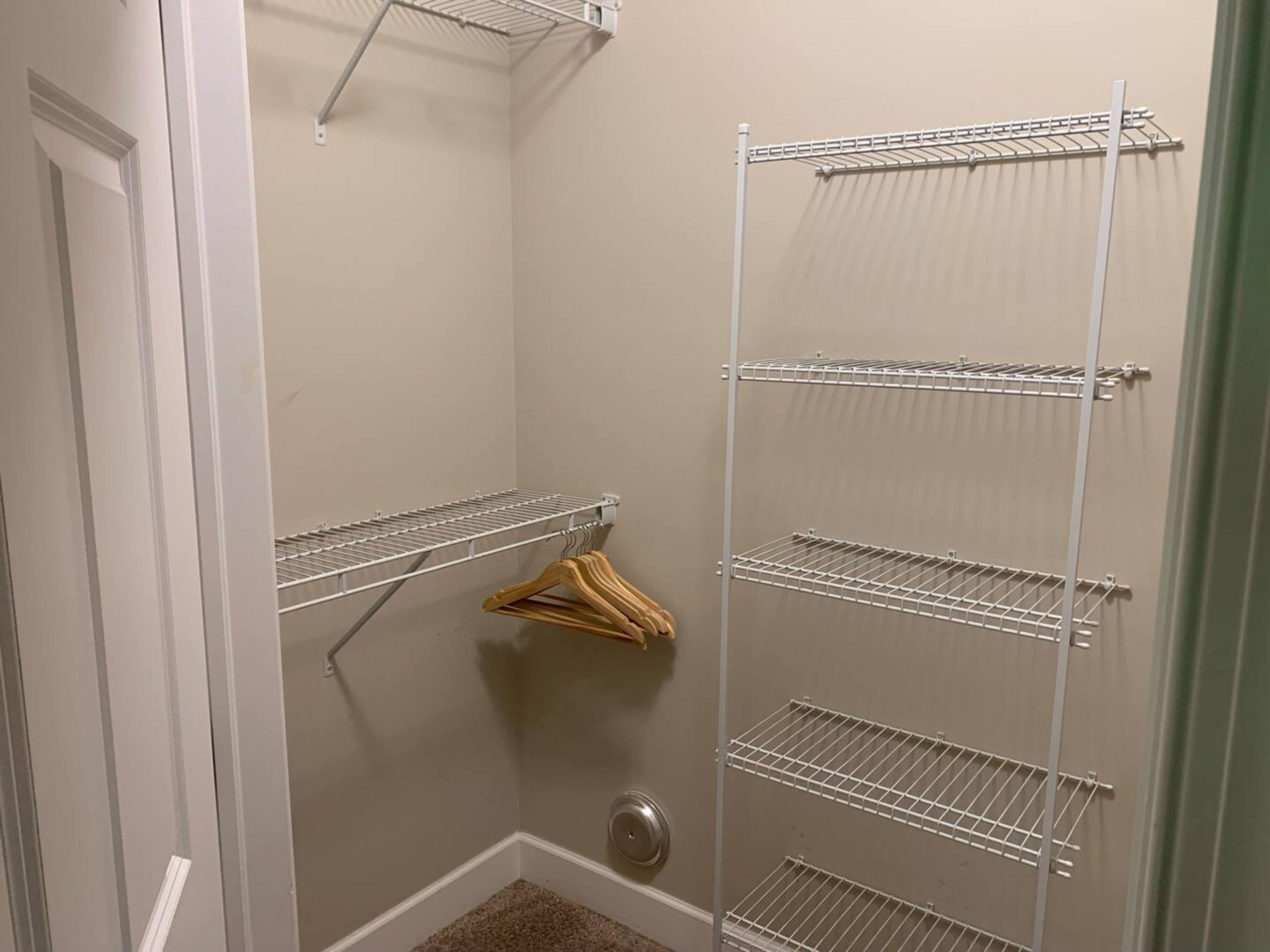 A walk-in closet with multiple metal wire shelves and a wooden hanger rack.