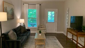 A living room with a sofa, a coffee table, a TV stand, and a door with a window. - Polaris King Flat Pet-friendly Nature Views (Westerville)
