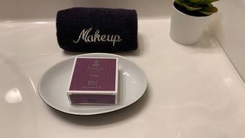 A bathroom with a white bathtub, a dark blue towel with "Makeup" embroidered, a small potted plant, and a white plate with a purple box.