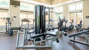 A gym with various exercise equipment, large windows, and a high ceiling.
