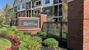 A sign for The Ravines at WESTAR, indicating a residential complex with brick and stone architecture, multiple balconies, and a well-maintained garden area.