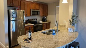 A modern kitchen with stainless steel appliances, wooden cabinets, granite countertops, and pendant lighting.