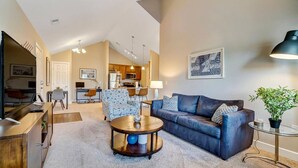 A modern living room with a sofa, coffee table, and a dining area in the background. - King Bed Top Floor Washer Dryer Balcony Wifi (Westerville)