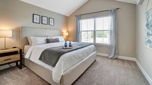 A bedroom with a large bed, two bedside tables, a window with curtains, and framed artwork on the wall. - King Bed Top Floor Washer Dryer Balcony Wifi (Westerville)