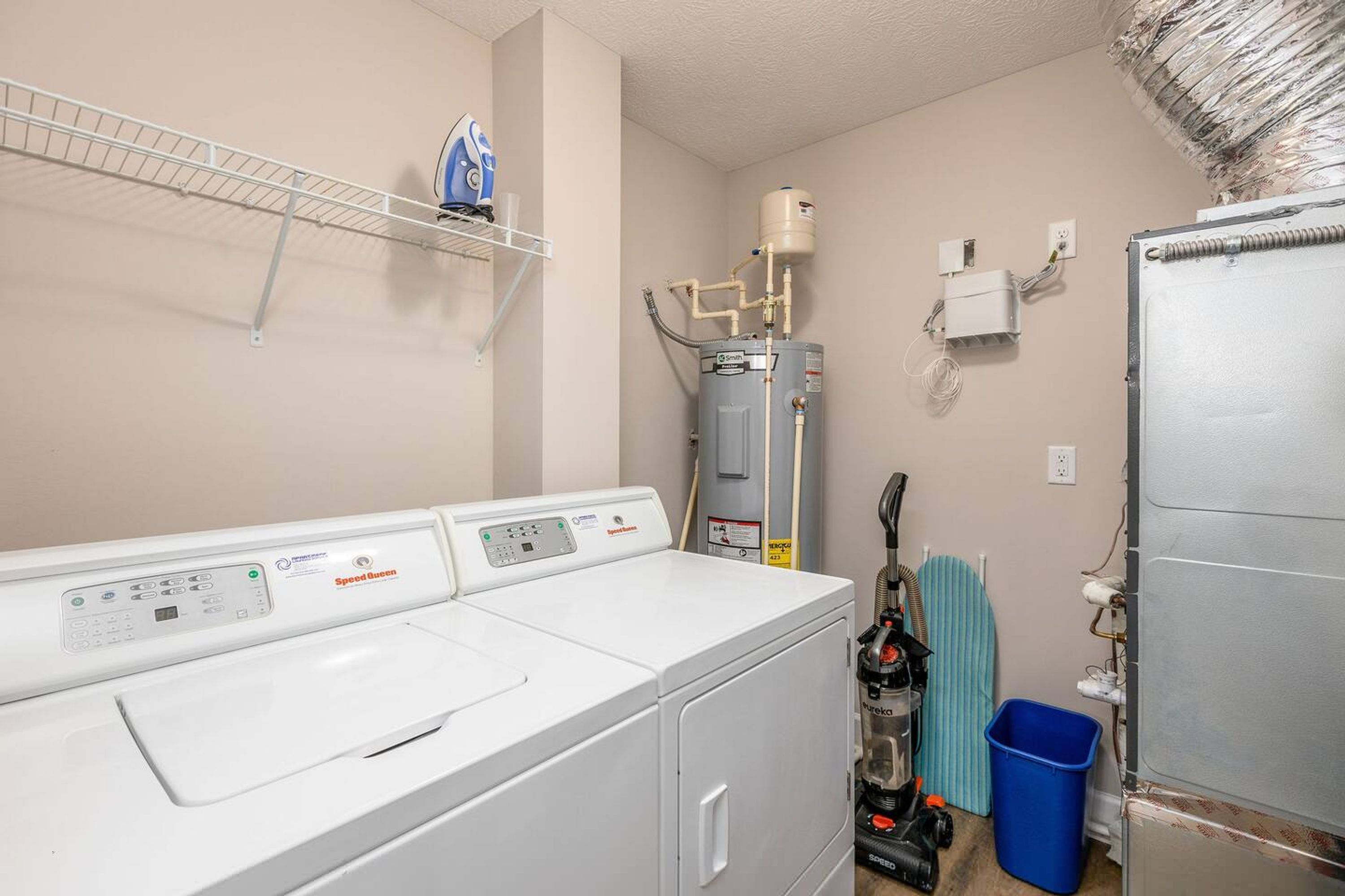 A laundry room with three stacked washers and dryers, a water heater, and a blue laundry basket.