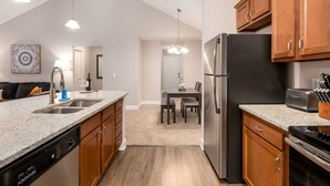 Una cocina moderna con encimeras de granito, electrodomésticos de acero inoxidable, armarios de madera y un comedor con lámpara de araña.