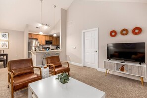 A modern living room with a white TV stand, leather chairs, a white table, and a kitchen in the background.