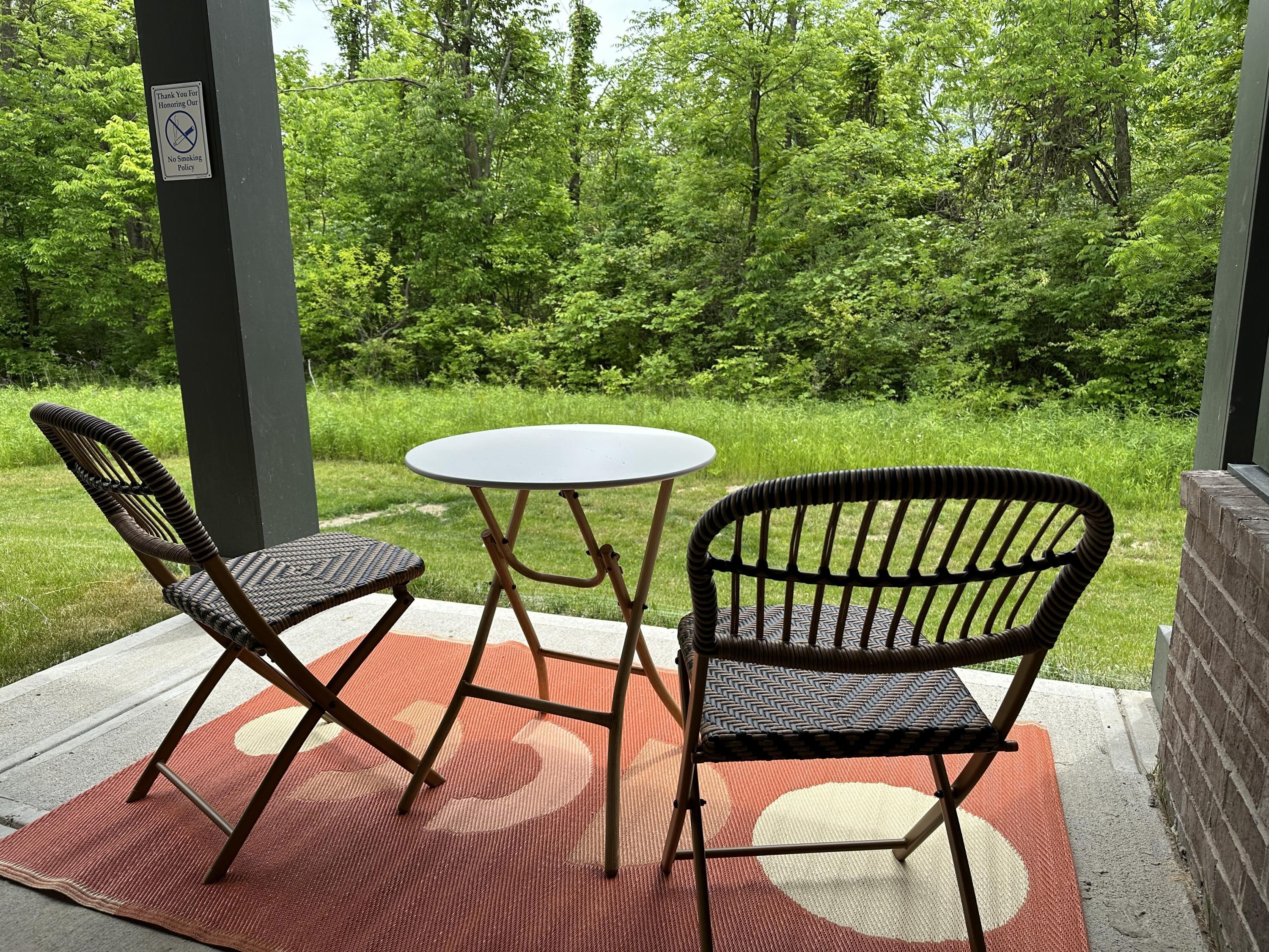 An outdoor seating area with two wicker chairs and a small round table, set on a patterned rug.