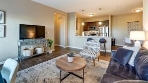 A modern living room with a flat-screen TV, a round coffee table, and a sofa. A kitchen area is visible in the background with a microwave and refrigerator. - Lux Dublin 2BR 1st Floor W D Pet Friendly (Dublin)