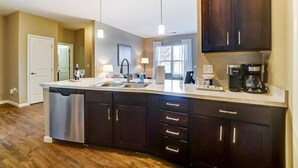 A modern kitchen with dark cabinetry, a central island with a dishwasher, a coffee maker, and pendant lighting. - Lux Dublin 2BR 1st Floor W D Pet Friendly (Dublin)