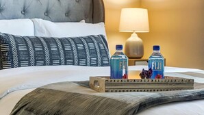 A hotel room with a tufted headboard, a bedside lamp, and a tray with two bottles of Fiji water. - Lux Dublin 2BR 1st Floor W D Pet Friendly (Dublin)